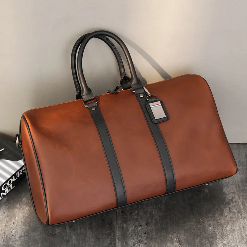 Brown leather duffel bag with black straps on a gray surface.