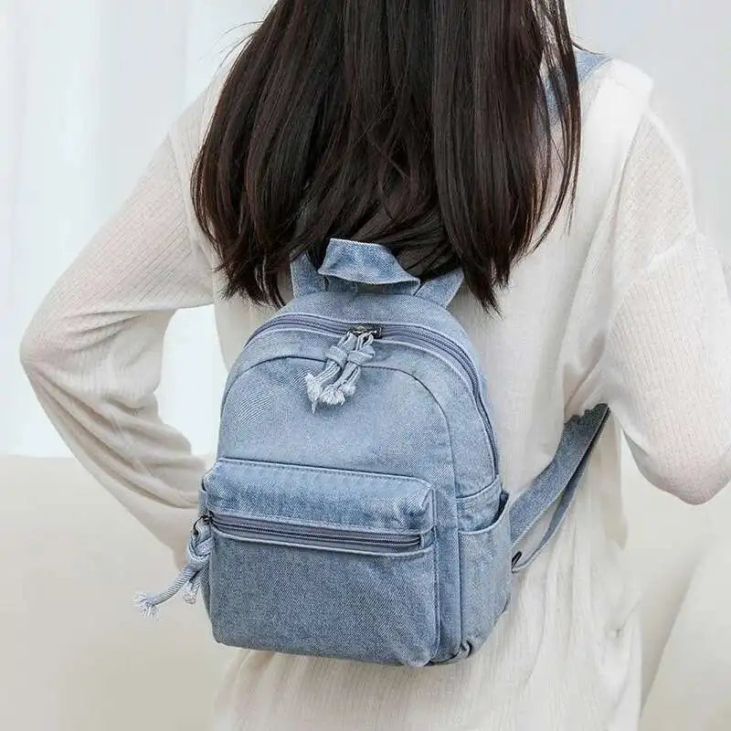 Person wearing a light blue denim backpack against a plain background