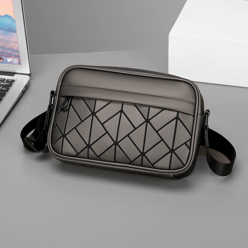 Gray crossbody bag with geometric pattern on a gray surface next to a laptop.