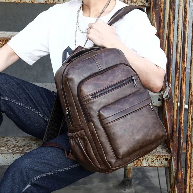 Person holding a brown leather backpack in an urban setting