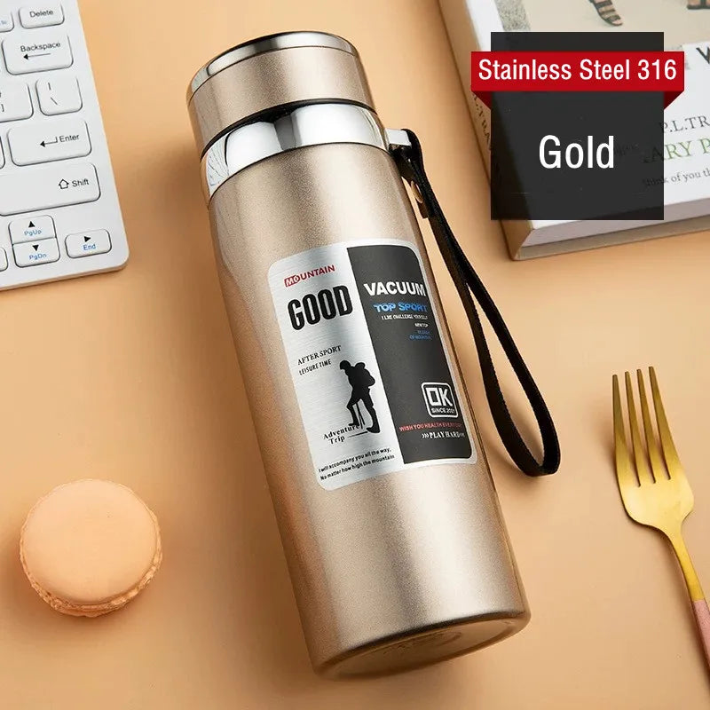 Gold stainless steel vacuum bottle with labels on a beige surface with a keyboard and fork.