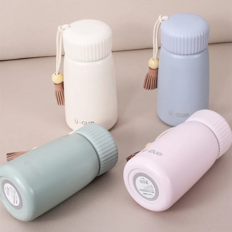 Four colorful thermos bottles with tassels on a neutral background