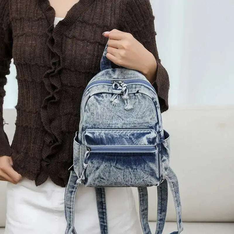 Person holding a blue denim backpack against a neutral background