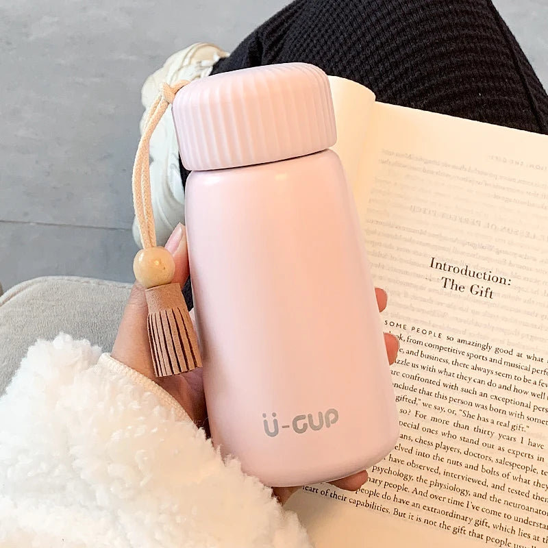 Pink travel mug held over an open book with a tassel bookmark.