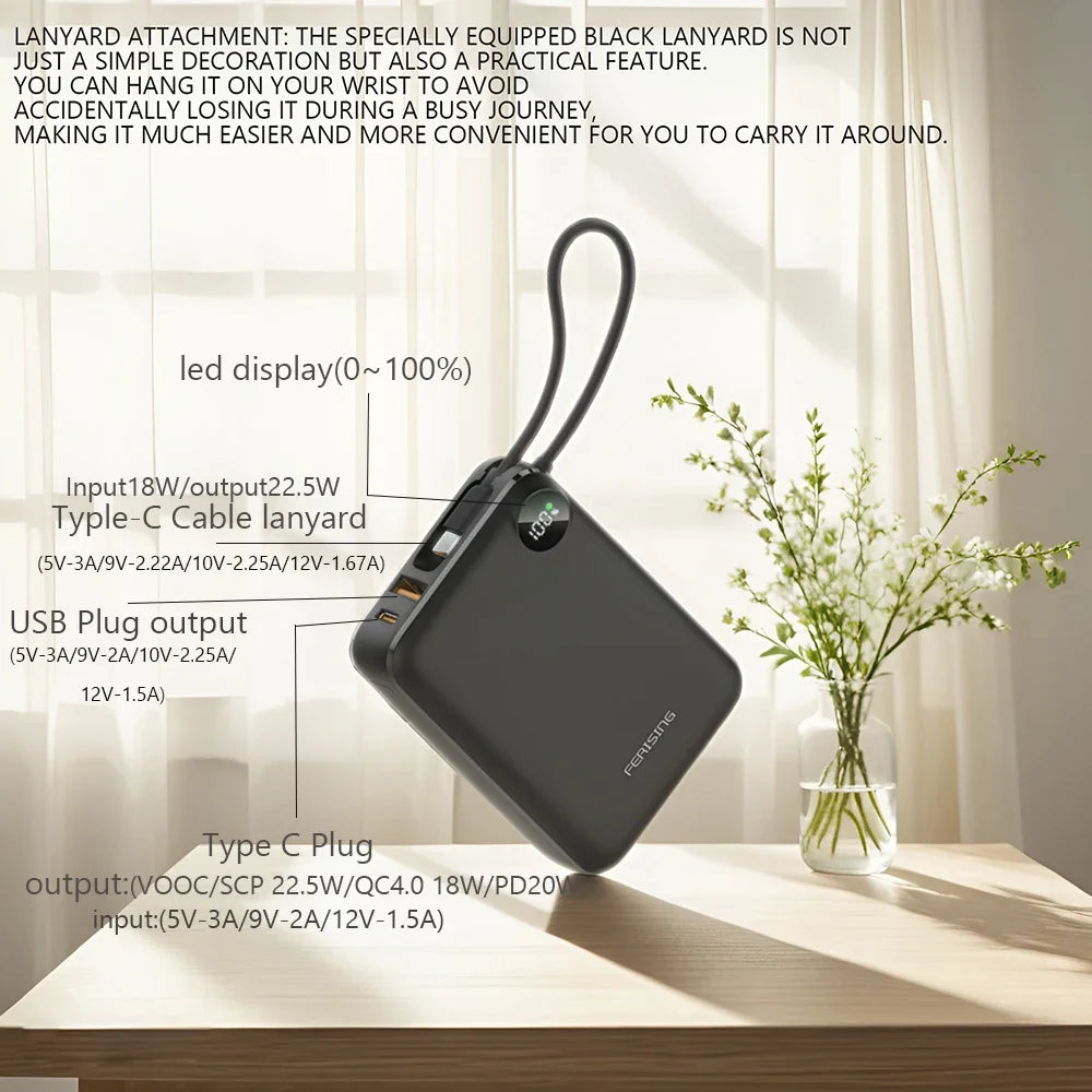 Black power bank with lanyard attachment on a table with a vase of flowers in the background