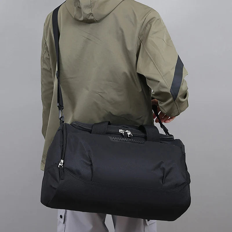 Person wearing a green jacket holding a black duffel bag against a gray background