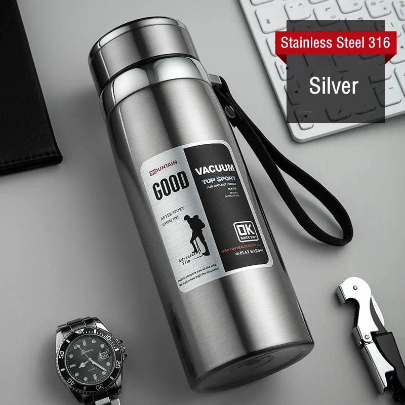 Silver vacuum flask withOK brand logo on a gray surface with keyboard and watch.