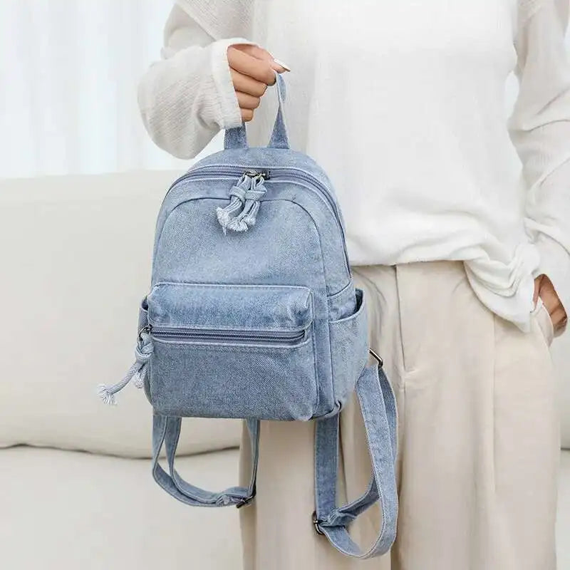 Light blue denim backpack held by a person against a white background