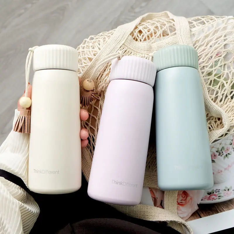 Three insulated bottles in white, pink, and light blue held against a textured surface.