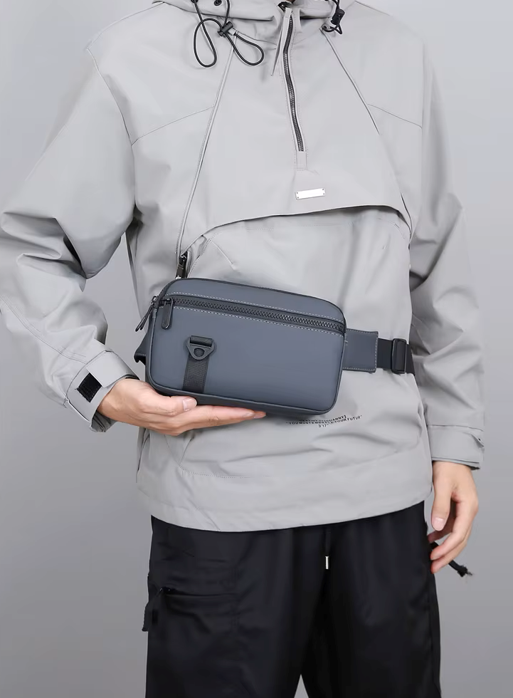 Person wearing a gray jacket holding a gray waist bag against a plain background