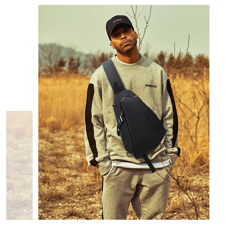 Man wearing a gray sweatshirt and pants with a black crossbody bag in a field.