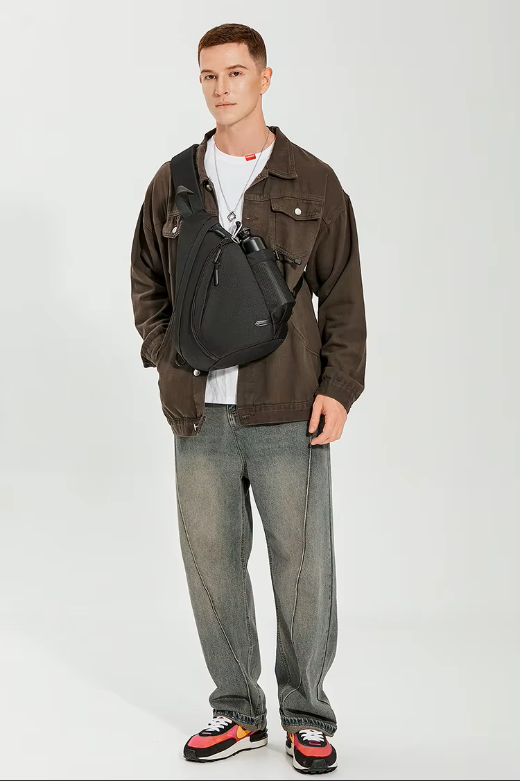 Man wearing a brown jacket, gray jeans, and black bag on a white background