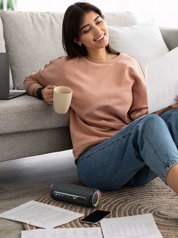 Woman sitting on a couch holding a mug, with a laptop and papers on the floor in front of her.