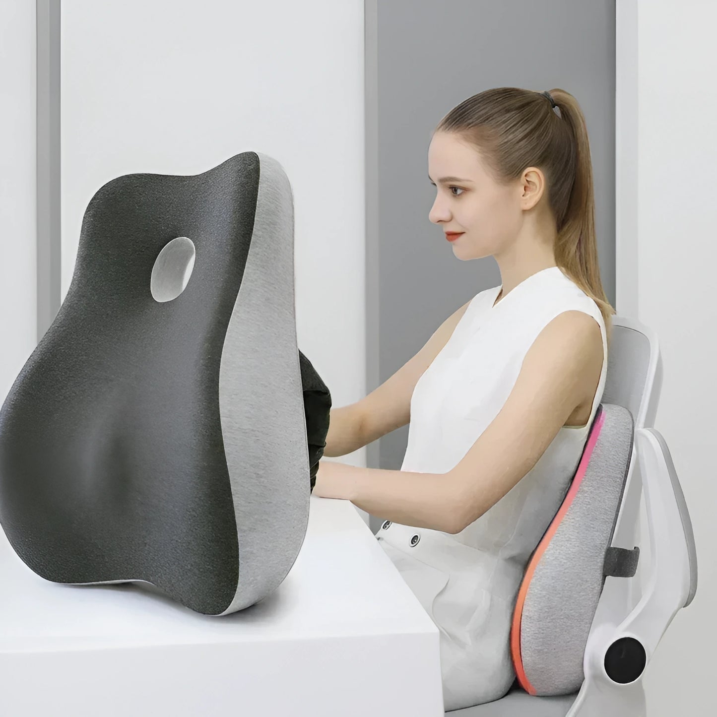 Woman using a gray and black ergonomic seat cushion on a white chair.