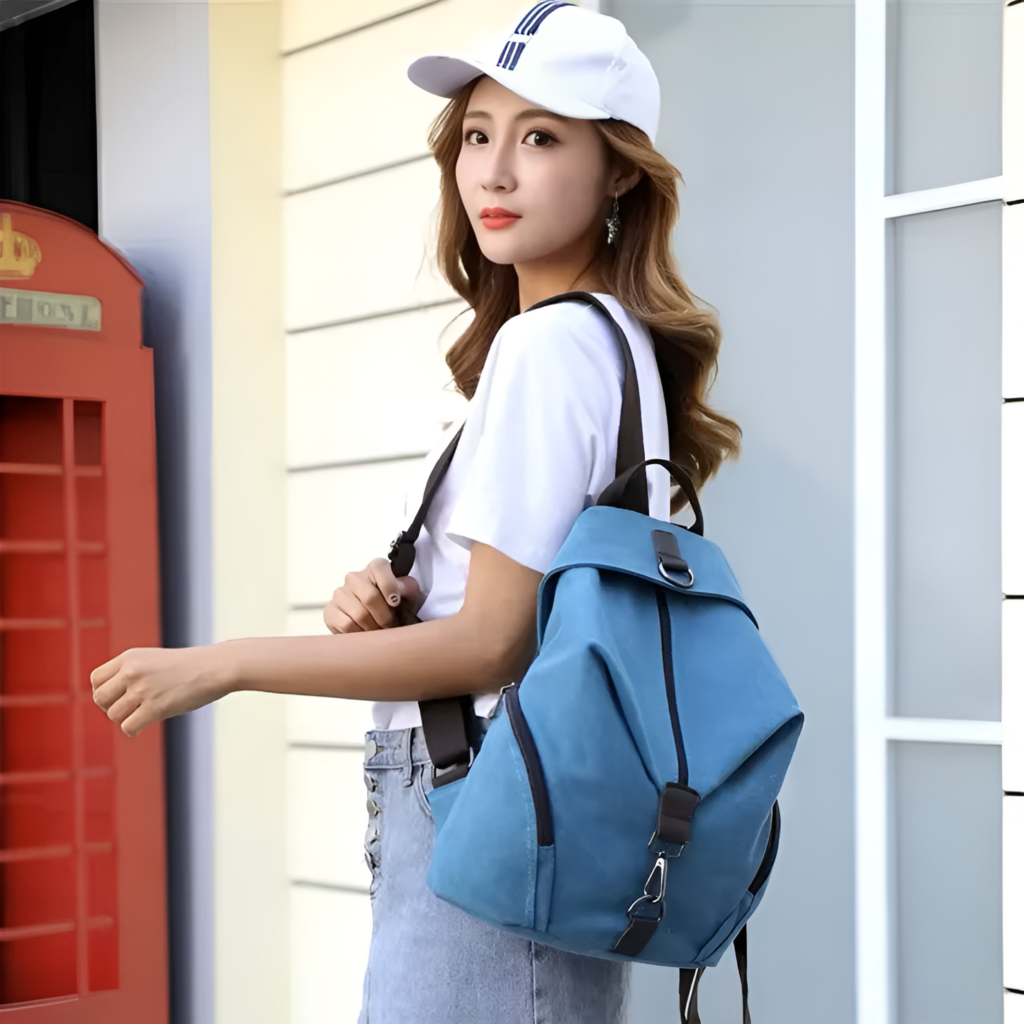 Woman wearing a white cap and blue backpack standing in front of a red telephone box.
