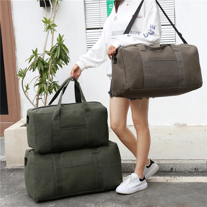 Person holding a large gray duffel bag with two green duffel bags on the ground.