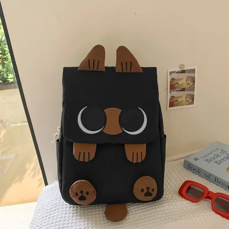 Black backpack with cat ears and face design on a surface.
