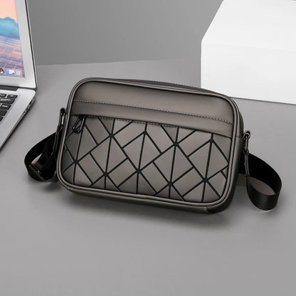 Gray crossbody bag with geometric pattern on a gray surface next to a laptop.
