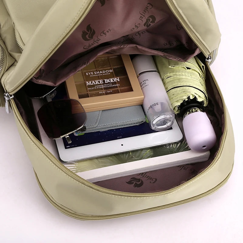 Open beige backpack with various items including a tablet, makeup products, and an umbrella.