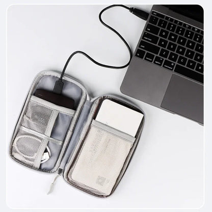 Travel organizer with USB cable, phone, and wallet next to a laptop on a white surface