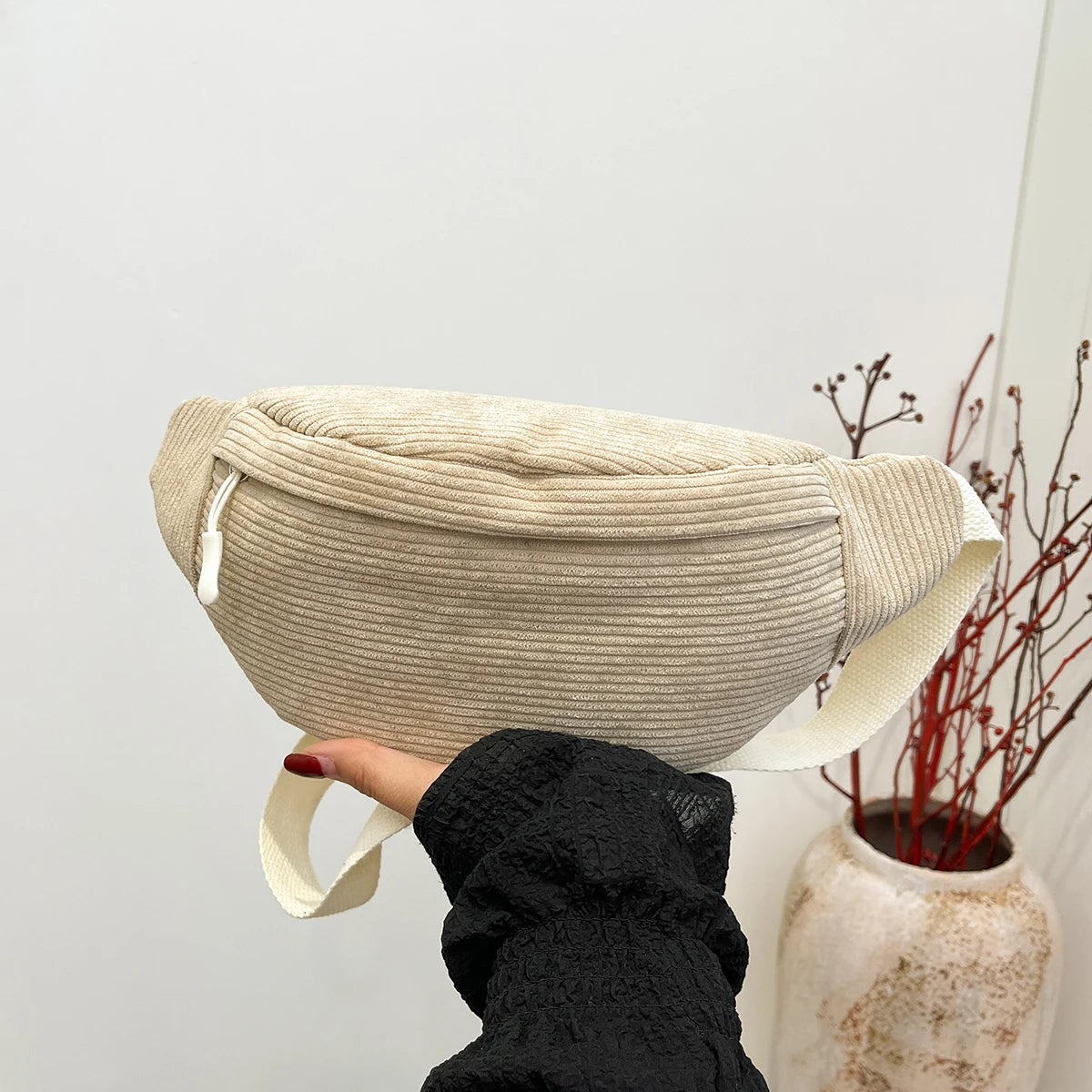 Beige woven belt bag held by a person with a neutral background