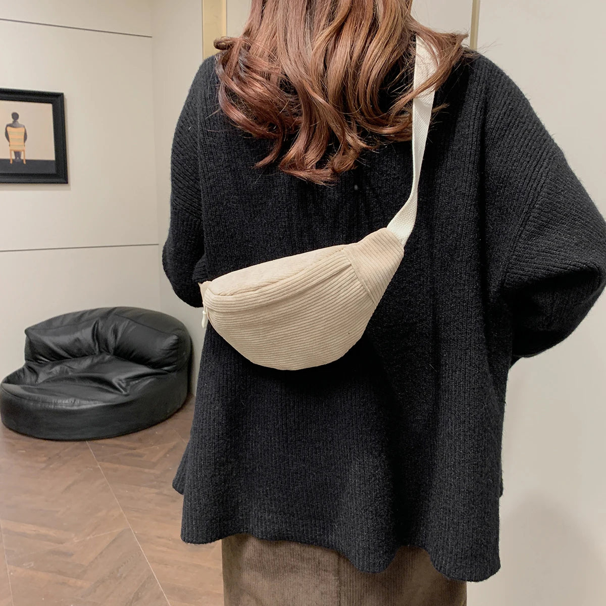 Person wearing a beige ribbed waist bag in an indoor setting