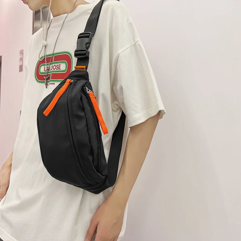 Person wearing a black crossbody bag with orange zippers and a white t-shirt with a logo.