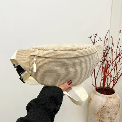Beige waist bag held by a person against a neutral background with a vase of red branches.