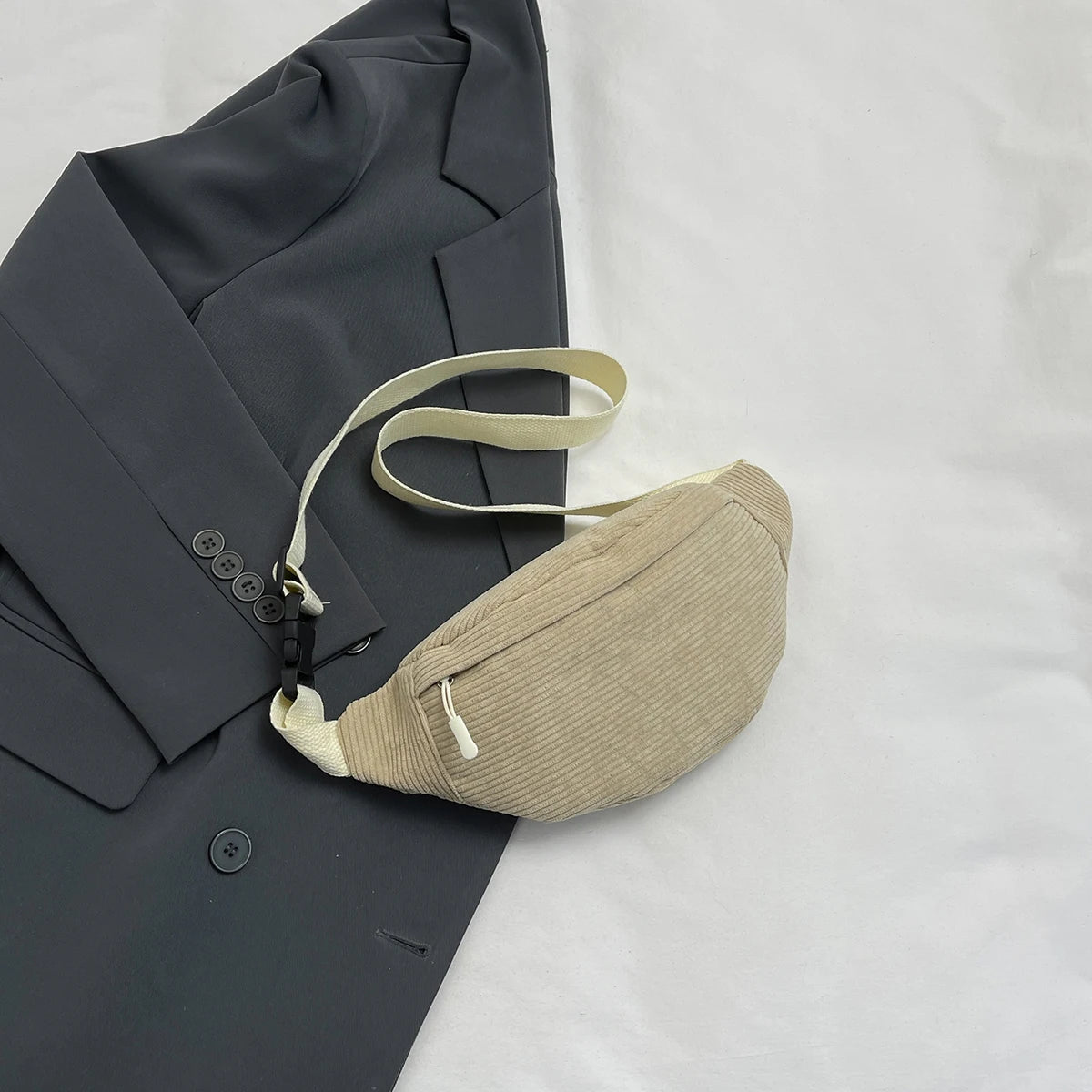 Beige waist bag on a dark gray suit jacket with a white background