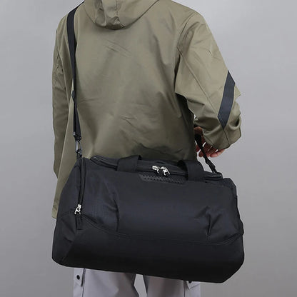 Person wearing a green jacket holding a black duffel bag against a gray background