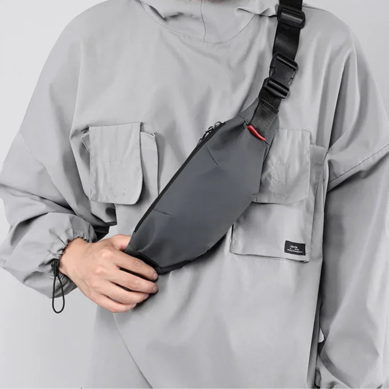 Person wearing a gray jacket holding a gray crossbody bag on a light gray background