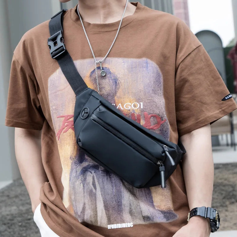 Person wearing a brown t-shirt with a graphic design and carrying a black crossbody bag.