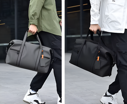 Two people carrying duffel bags, one gray and one black, on a city street.